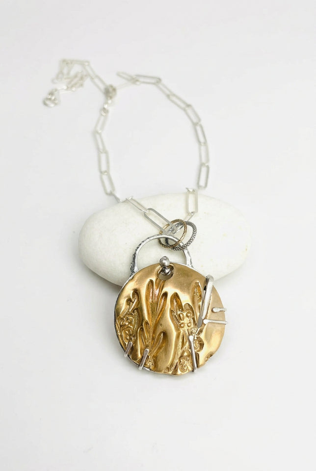 A silver paper clip chain necklace with a round pendant featuring a textured bronze cherry blossom design wrapped in silver wire, displayed on a white background with a small white stone.