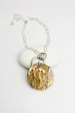 A silver paper clip chain necklace with a round pendant featuring a textured bronze cherry blossom design wrapped in silver wire, displayed on a white background with a small white stone.