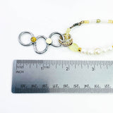 Necklace with circular pendant and beads next to a ruler for scale on a white background