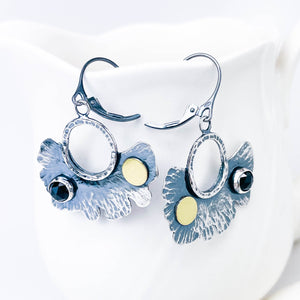 Pair of silver earrings with black spinel and gold accents on manequin