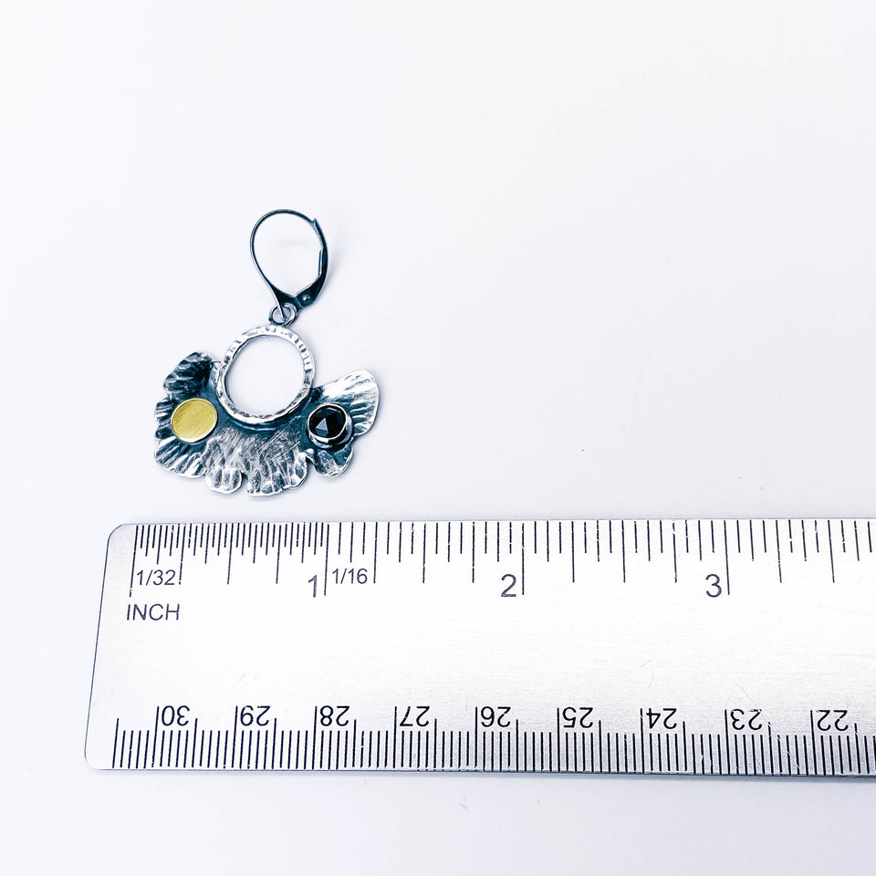Pair of silver earrings with black spinel and gold accents on handcrafted leaf with ruler depicting measurement.  