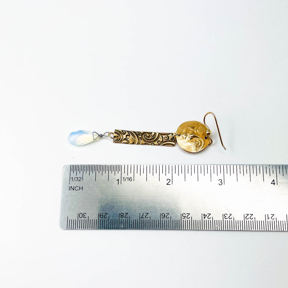 Bronze earring with a clear translucent gemstone (opalite) next to a ruler on a white background