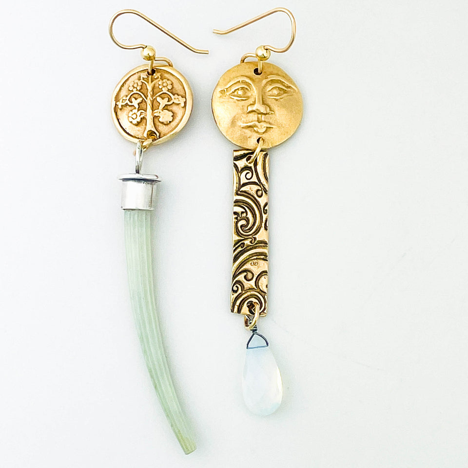 Bronze and silver earrings with face design and tusk shell on a white background