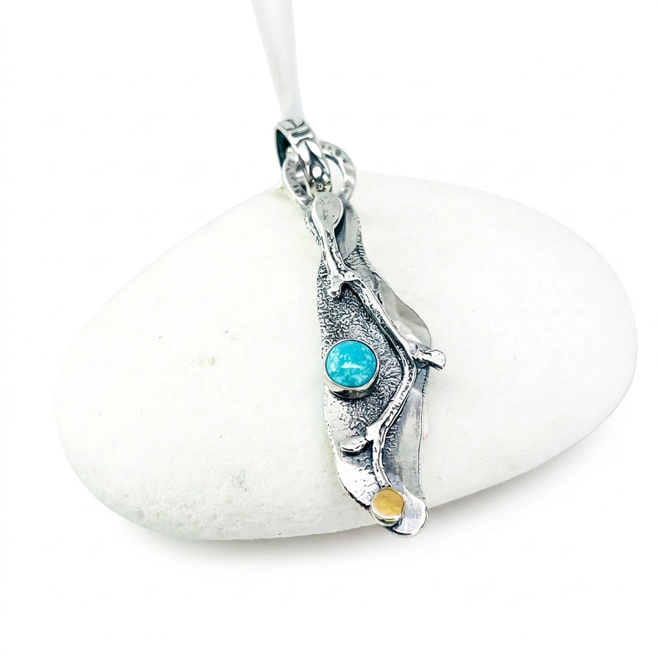 A textured sterling silver pendant necklace with organic leaf-like curves, featuring a small round turquoise blue gemstone and a tiny gold accent, displayed on a smooth white stone against a white background.