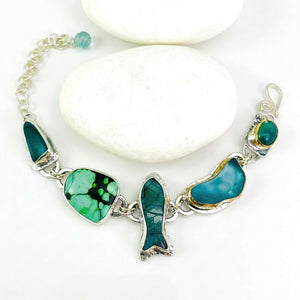 A woman wearing a bohemian-style turquoise and silver charm bracelet, shown in a warm, sunlit outdoor setting with blurred plants in the background.