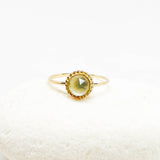 A gold ring with a round faceted light moonstone gemstone, displayed on a white textured stone against a white background.
