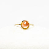 A gold ring with a round faceted rose quartz gemstone, displayed on a soft white textured surface.